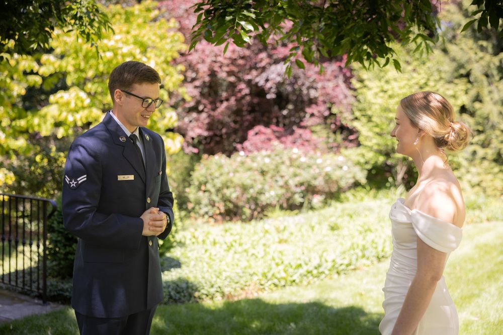 Groom in military uniform shares a first look moment with bride in white gown in a lush garden setting.
