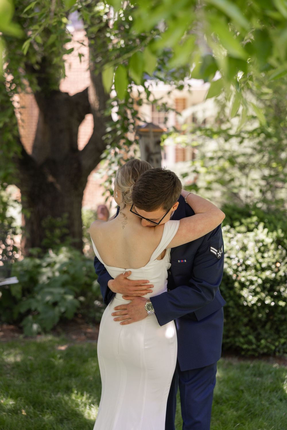 A bride and groom share a tender embrace in a lush garden, with the bride in a white gown and groom in a navy suit.