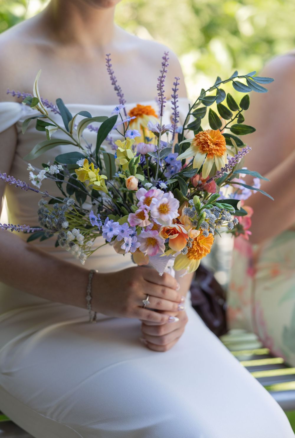 Bride in white dress holding a colorful wildflower bouquet with orange, purple, and blue blooms at a wedding.
