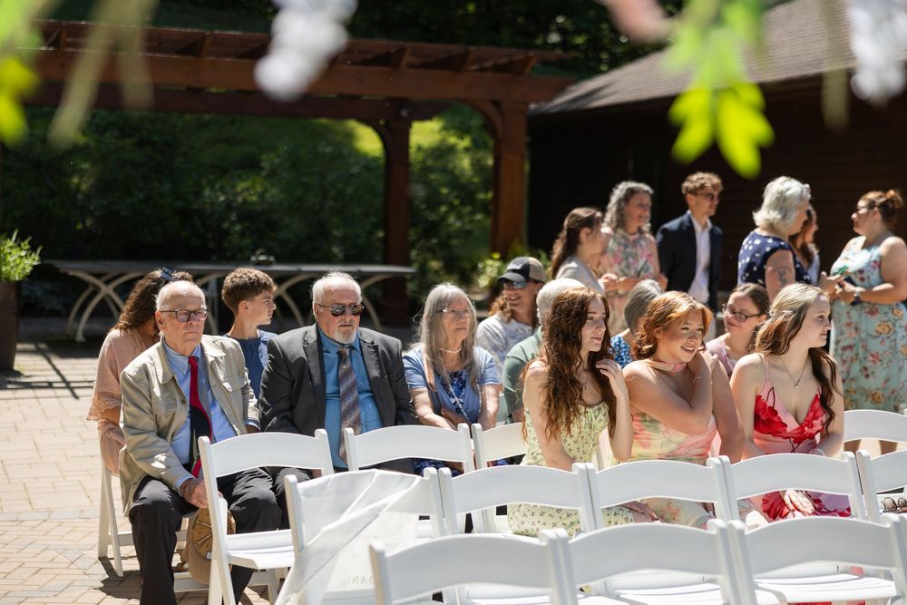 Guests seated in white chairs at an outdoor wedding ceremony on a sunny day.