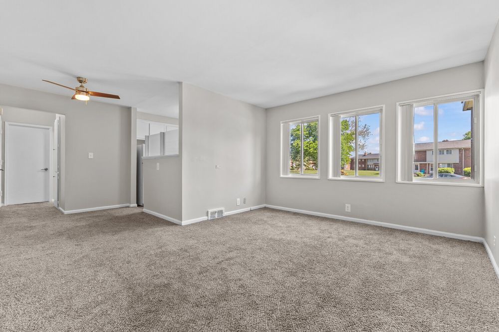 Bright living room with beige carpet, ceiling fan, and large windows offering natural light in a modern home.