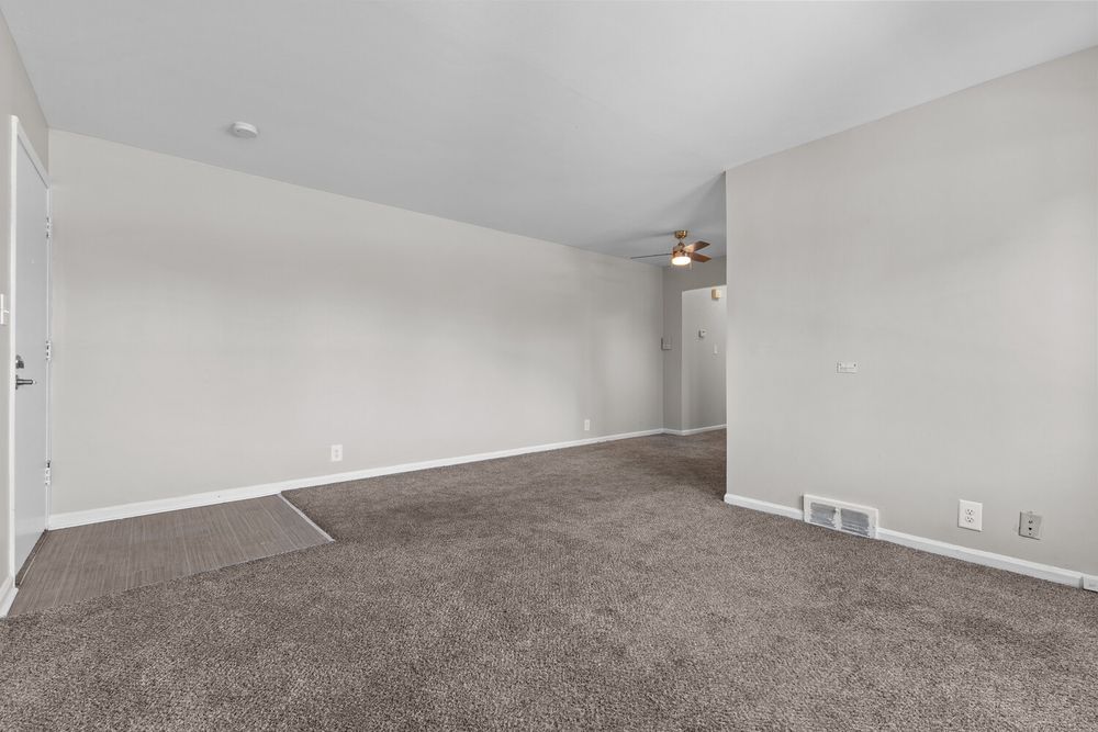 Empty carpeted living room with ceiling fan, neutral walls, and visible doorways in a bright, move-in ready home.