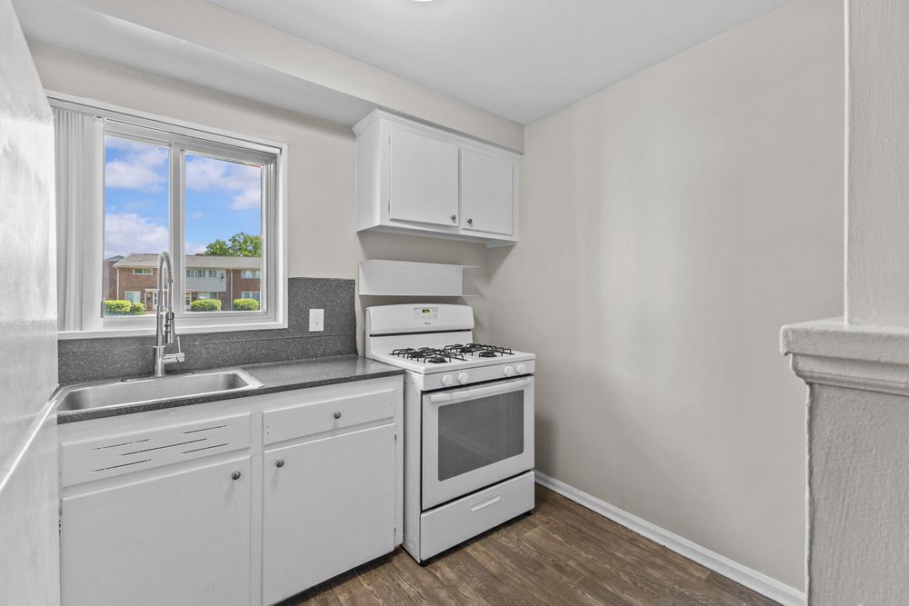 White kitchen with gas range, sink, white cabinets, and dark wood flooring near a bright window.