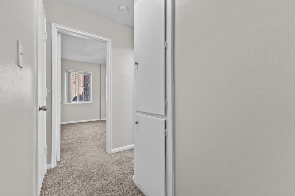 Narrow hallway with beige carpet, white walls, and open doors leading to additional rooms in a residential home.