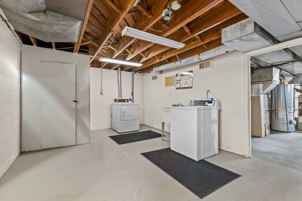 Unfinished basement laundry area with washer, dryer, white storage cabinets, exposed ceiling beams, and painted concrete floors.