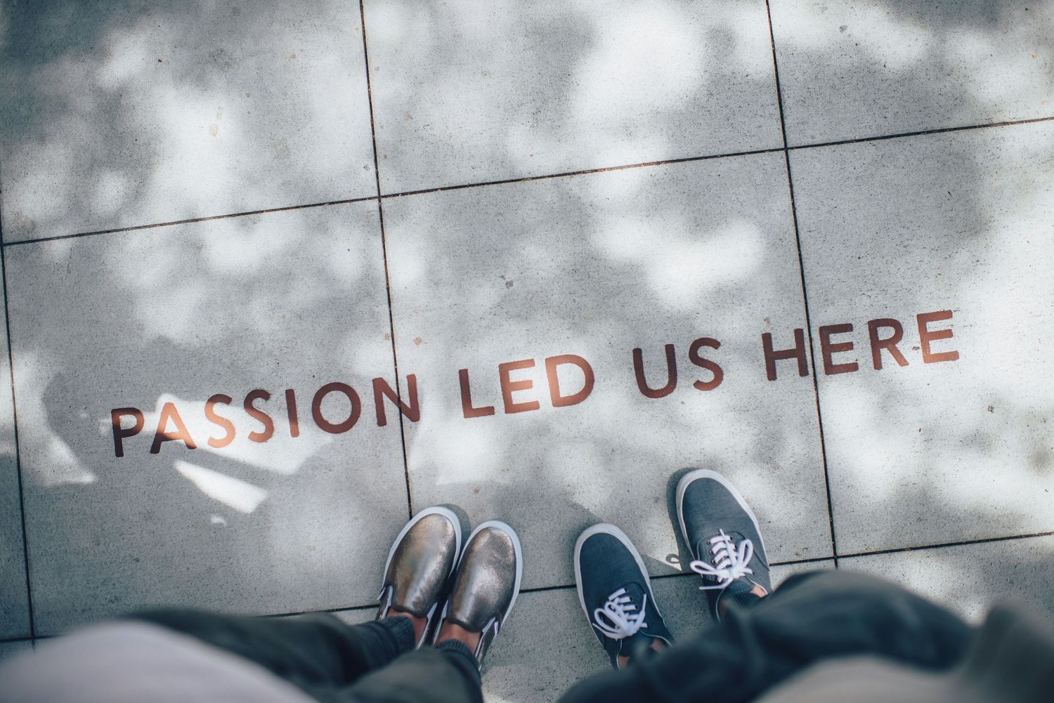 Two people standing on a tiled floor with 'Passion Led Us Here' inscription, viewed from above.