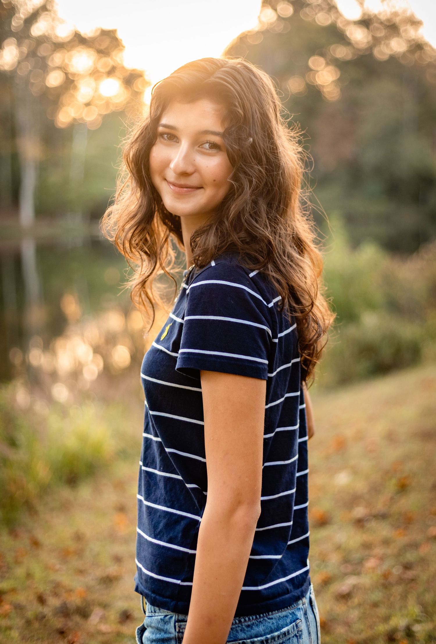 A young woman in a blue, striped shirt is framed by a warm autumnal glow for her Charlottesville senior photography session.