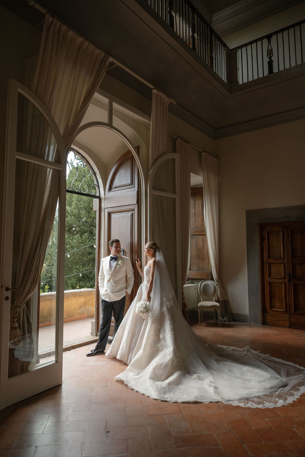 Bride and groom share a romantic moment in an elegant villa with arched doors and terracotta floors.