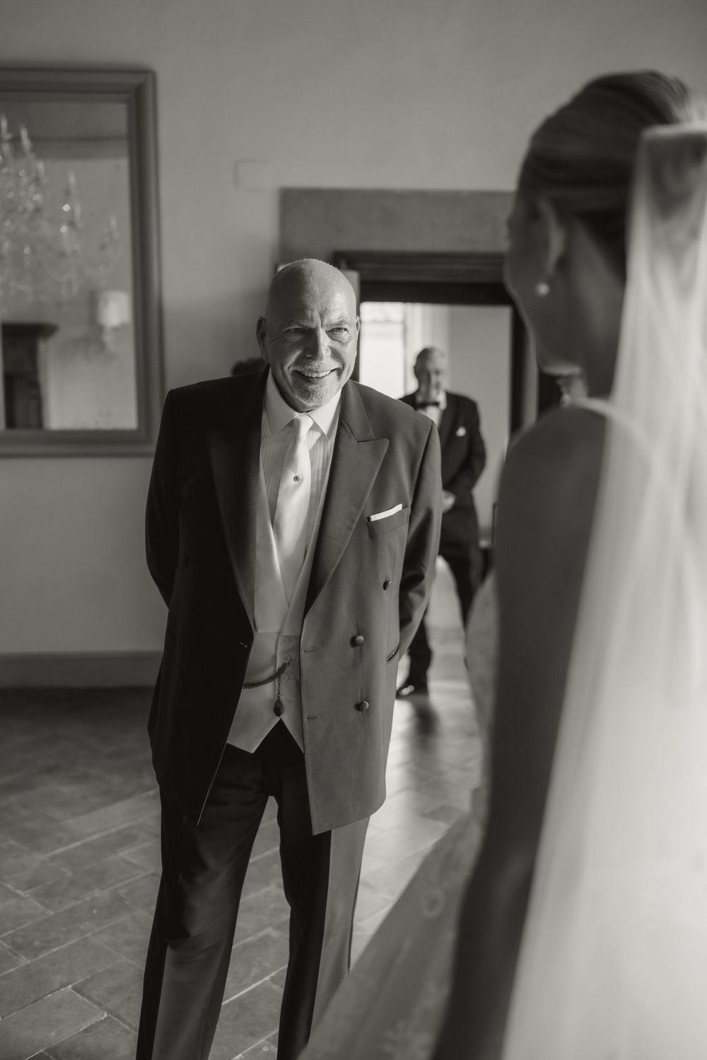Black and white photo of a smiling father in a tuxedo seeing his bride daughter for the first time on wedding day.