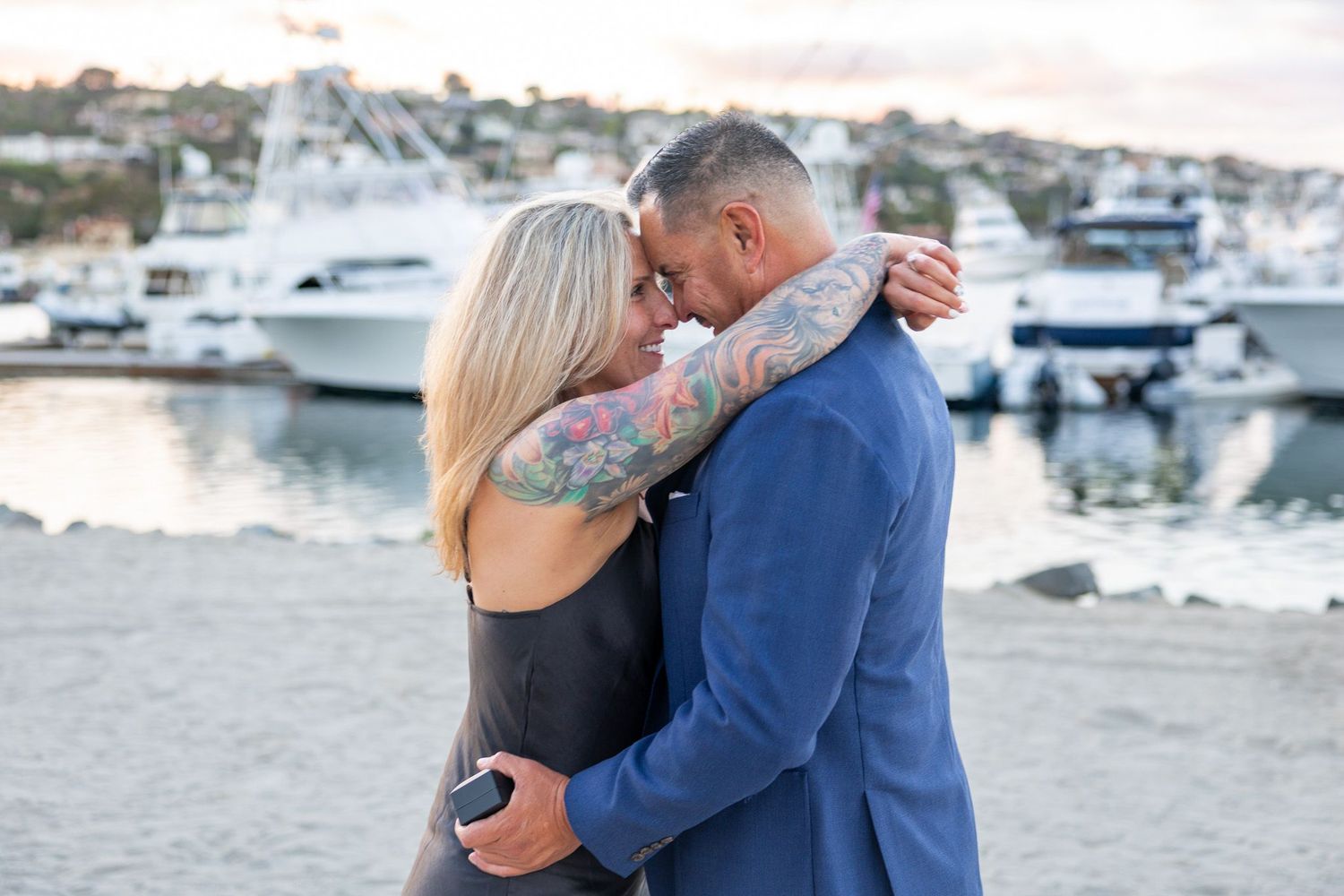 San Diego engagement photography of a newly engaged couple embracing at a harbor marina with boats in the background.
