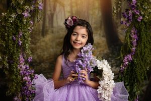 A person in a purple dress poses among blooming wisteria vines in a dreamy garden setting.