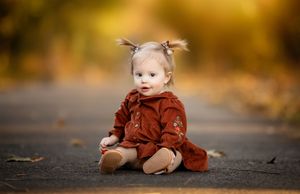 A series of autumn-themed photos showing a small figure in a rust-colored dress sitting on a path with golden leaves.