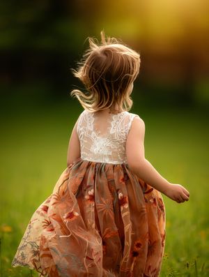 A young girl in a floral dress twirls in a sunlit green meadow, her hair flowing in the breeze.