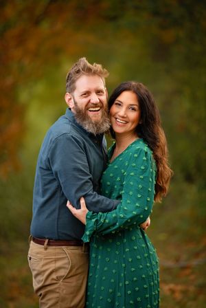 A couple embraces and laughs together while wearing green and navy outfits during an autumn outdoor photoshoot.