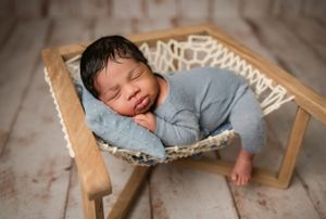 Peaceful newborn sleeping in a hammock wearing light blue sleepwear during professional photo session.