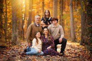 A family sits together on fallen autumn leaves in a golden sunlit forest during a photo session.
