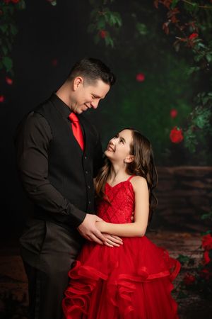 A heartwarming moment captured in formal wear against a dark backdrop with red floral accents.