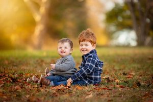Children playing and laughing together in fallen autumn leaves during a golden sunset photo session.