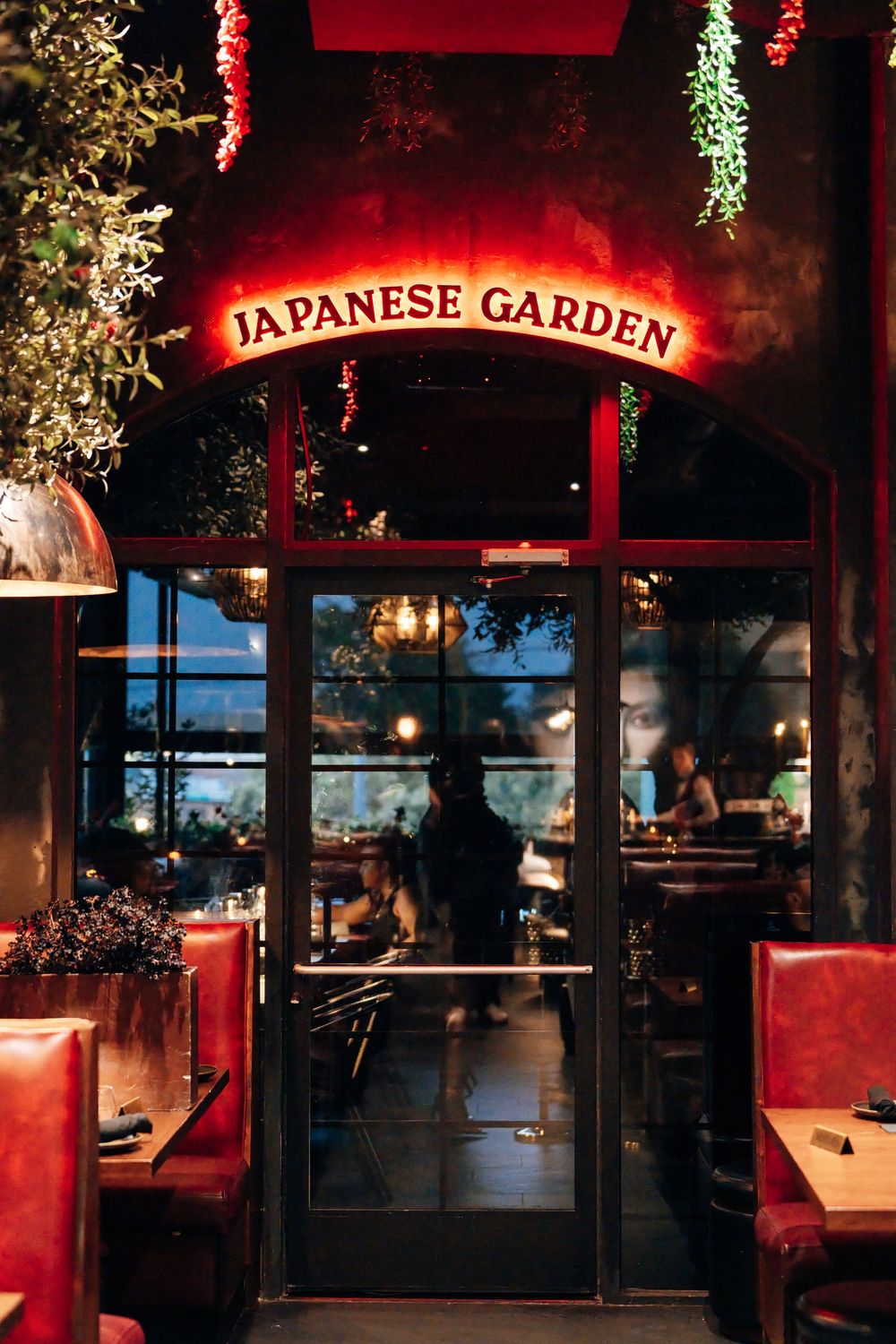 Glowing red neon Japanese Garden sign above a glass door entrance, with red leather booths and diners visible inside the restaurant.