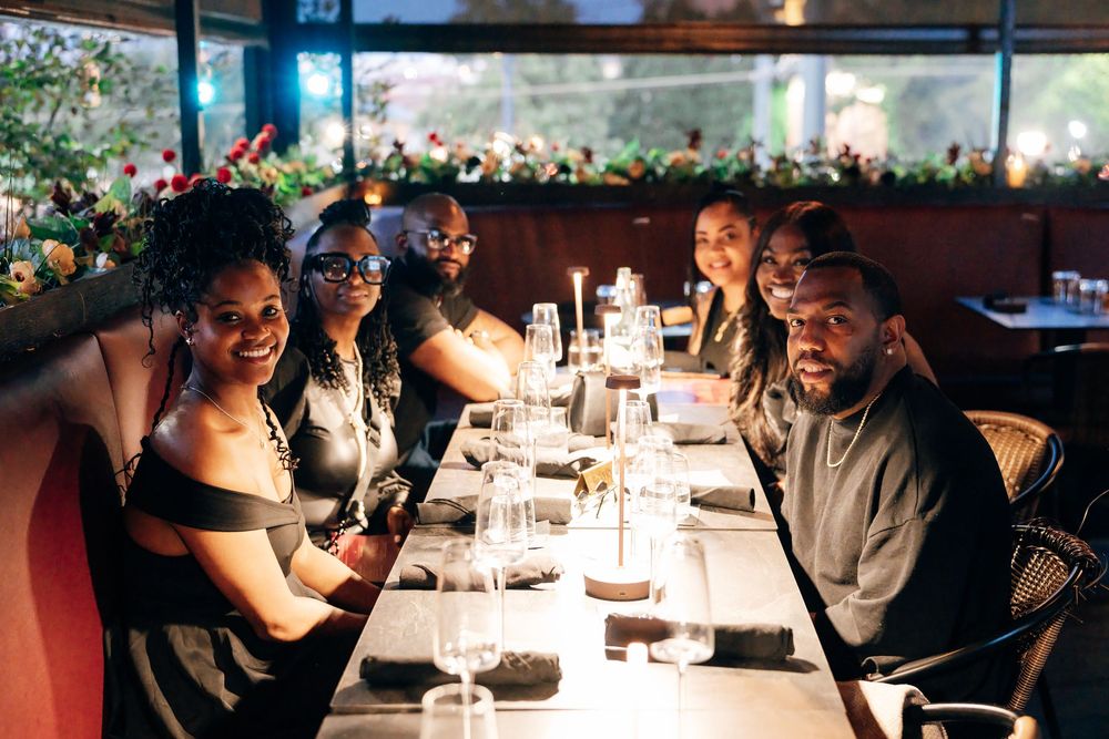 Group of friends smiling together at a long candlelit dinner table in an elegant restaurant decorated with festive flowers.