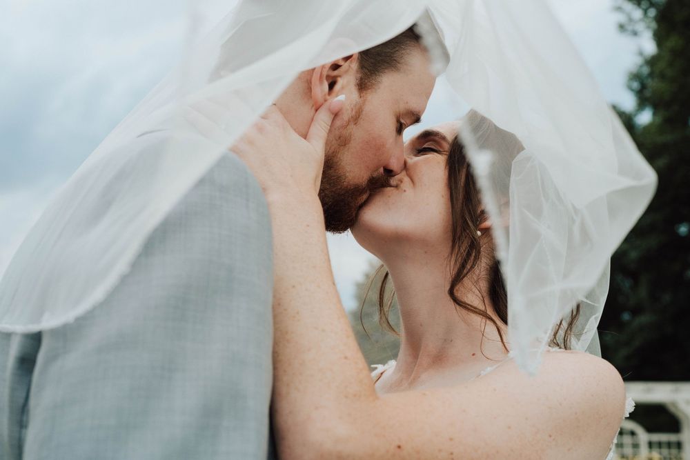 Bride and groom sharing a romantic kiss under a flowing white veil on their wedding day.
