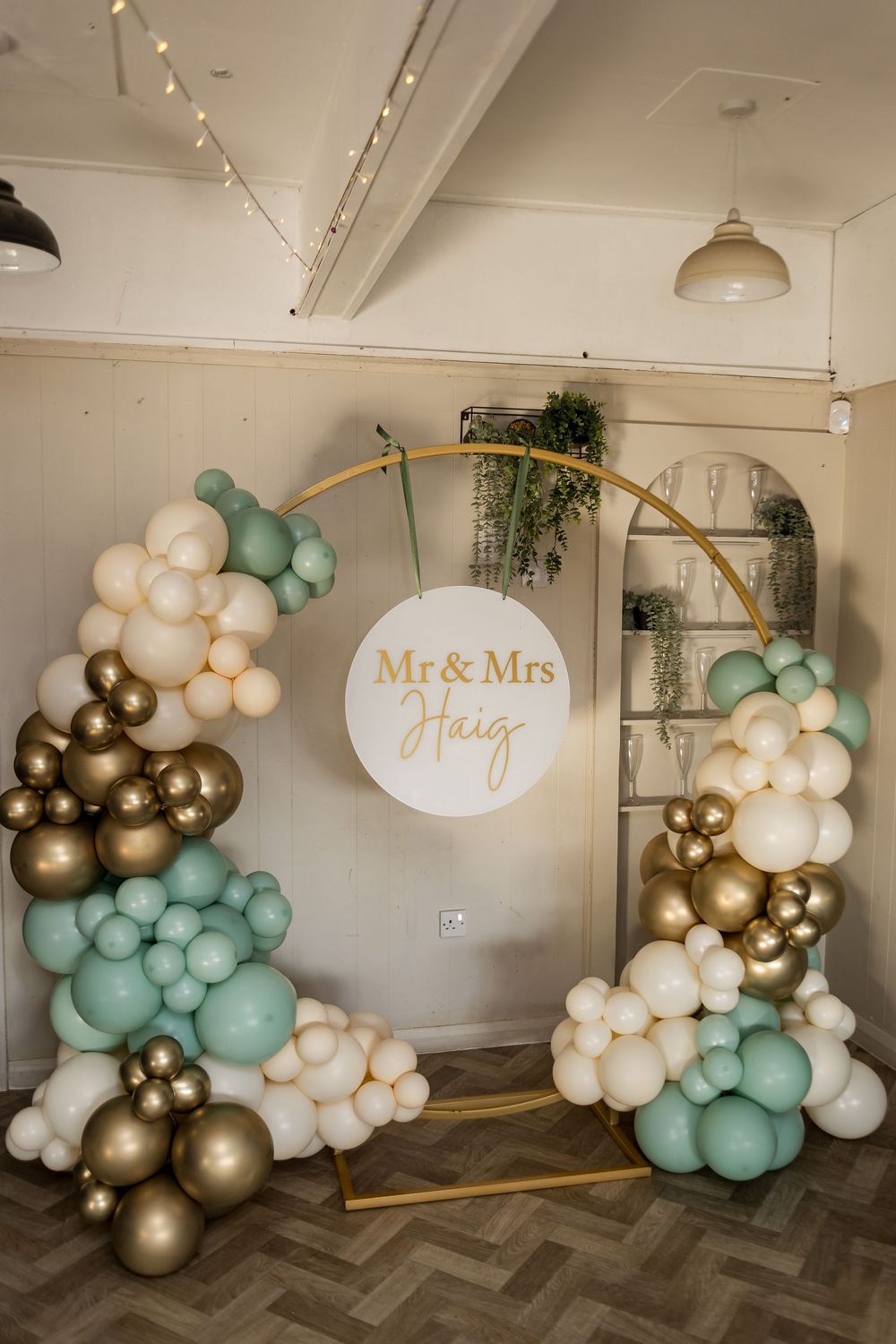 Elegant wedding balloon arch with sage green, gold, and ivory balloons framing a Mr & Mrs Haig circular sign.