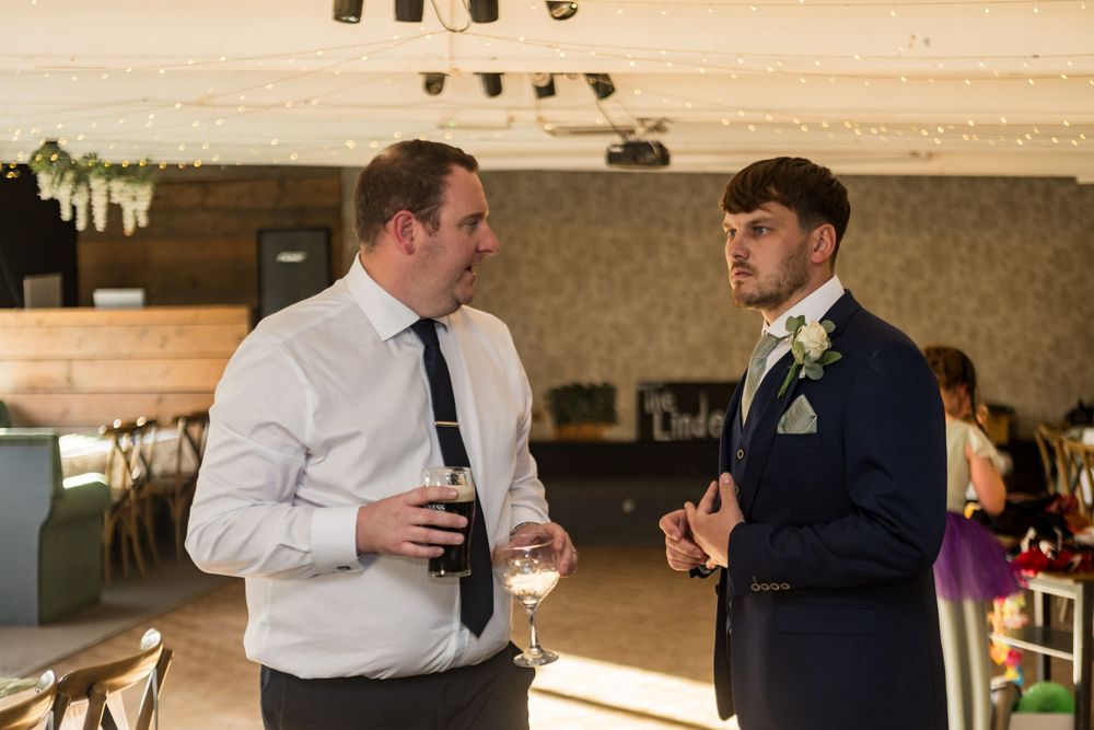 Two men in formal attire having a conversation at a wedding venue reception.