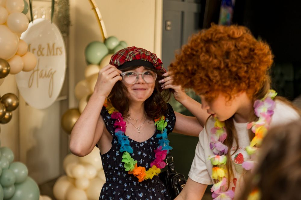 Woman trying on a cap at a wedding photo booth with colorful balloon decorations.