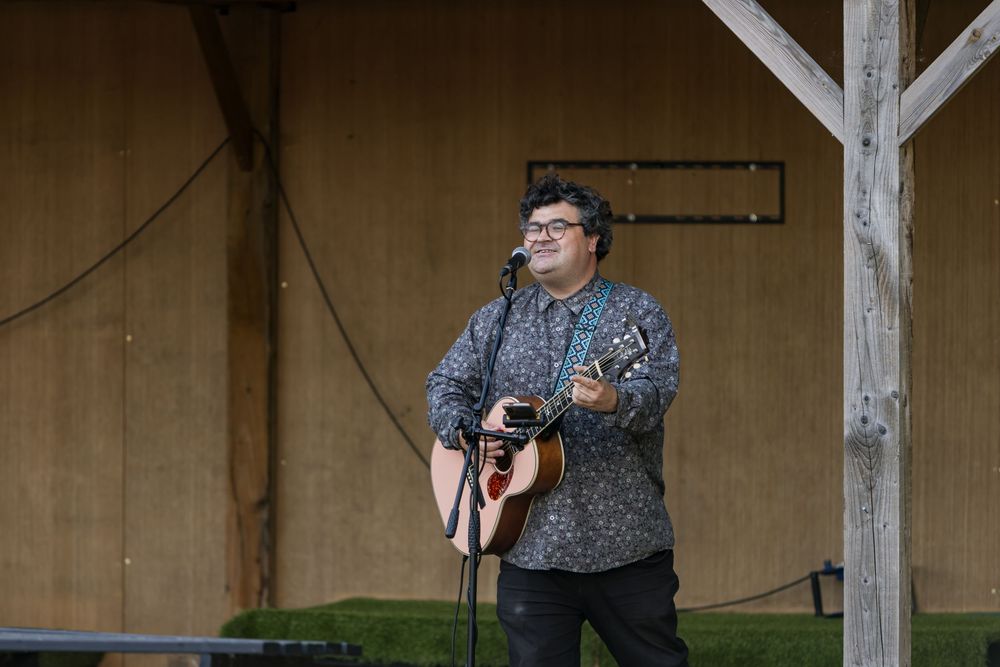 A man playing acoustic guitar and singing on an outdoor stage at a live music event.