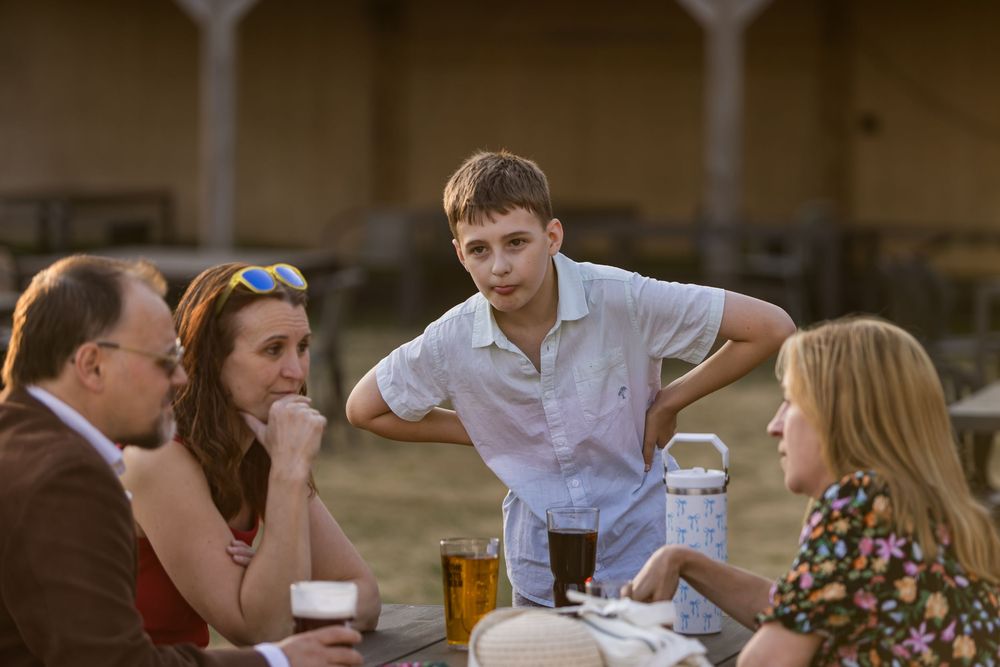 Four wedding guests converse around a wooden table at an outdoor reception in golden hour light.