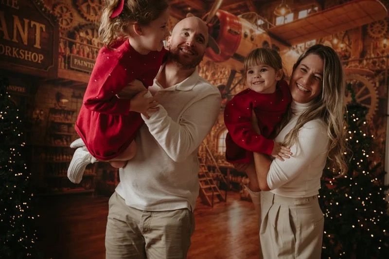 Parents smiling with their two children during a previous Christmas photography session.