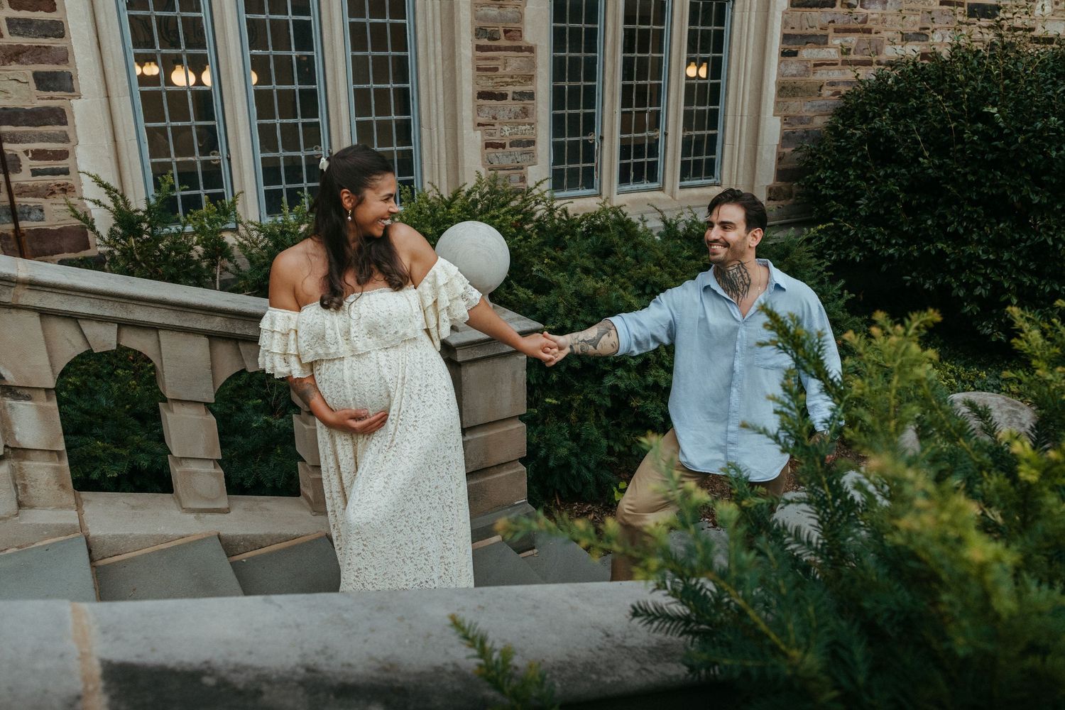 Pregnant mom in a white lace dress reaching for her partner on a stone terrace, Central NJ maternity photos