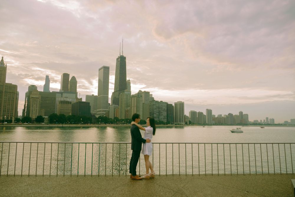 Couple embracing on Chicago waterfront with iconic city skyline and John Hancock Center in background at dusk.