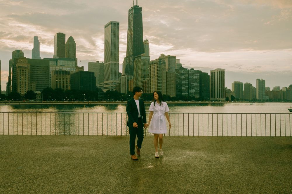 Couple walking along Chicago waterfront with city skyline backdrop at dusk.