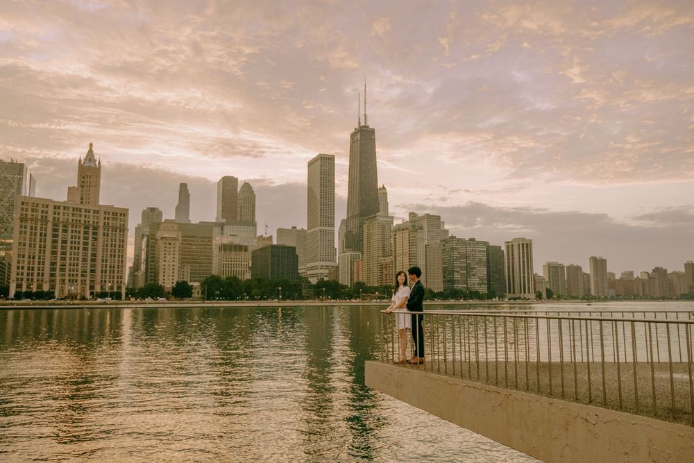 Couple embracing on Chicago waterfront at sunset with iconic Willis Tower skyline reflecting golden light over Lake Michigan.