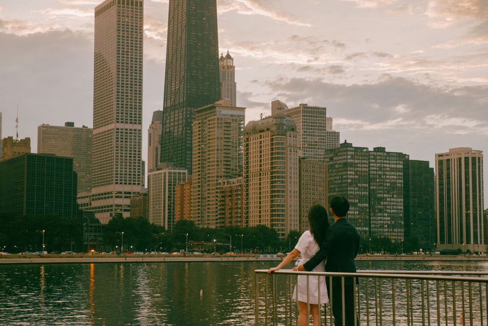 Couple standing at a railing overlooking the Chicago skyline and lake at sunset.