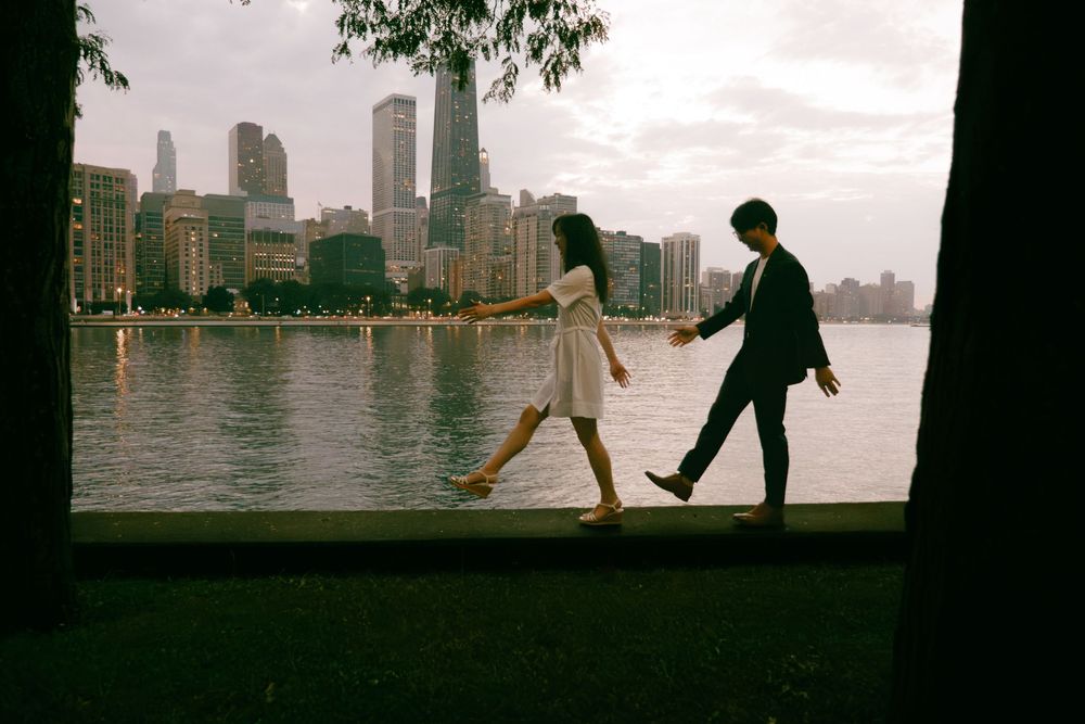 Couple holding hands walking by a city waterfront at dusk with skyscrapers in the background.