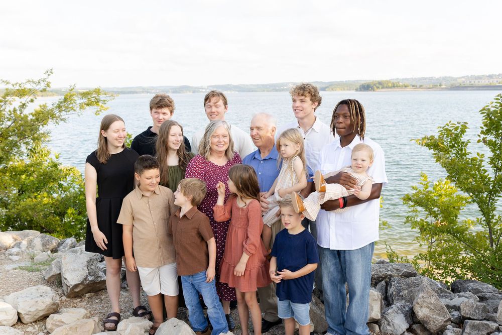 Multi-generational family posing on rocky lakeside, smiling together outdoors.