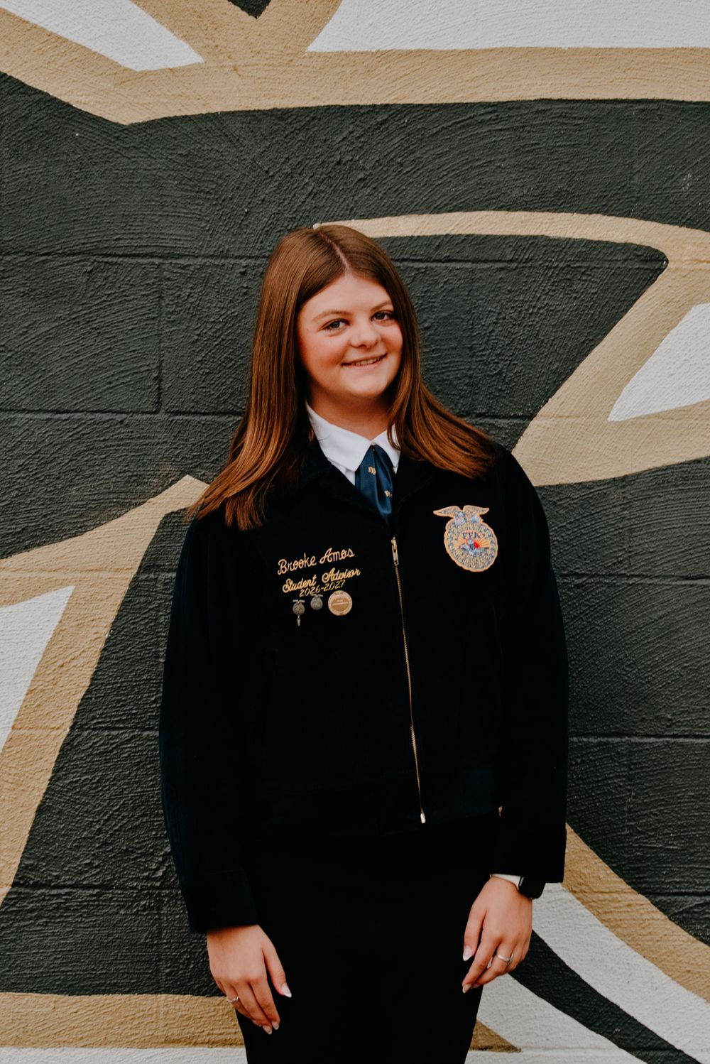 Young woman in FFA official dress jacket smiling confidently against a painted wall backdrop.