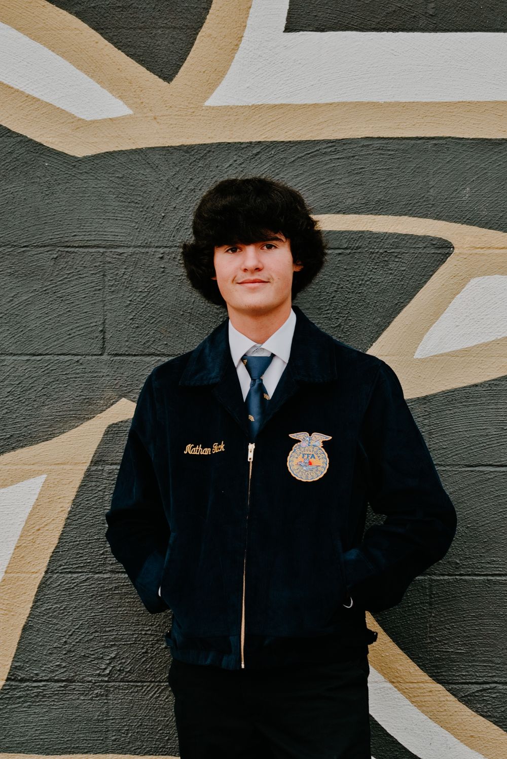 Teen in FFA navy jacket with emblem poses confidently against a colorful mural wall.
