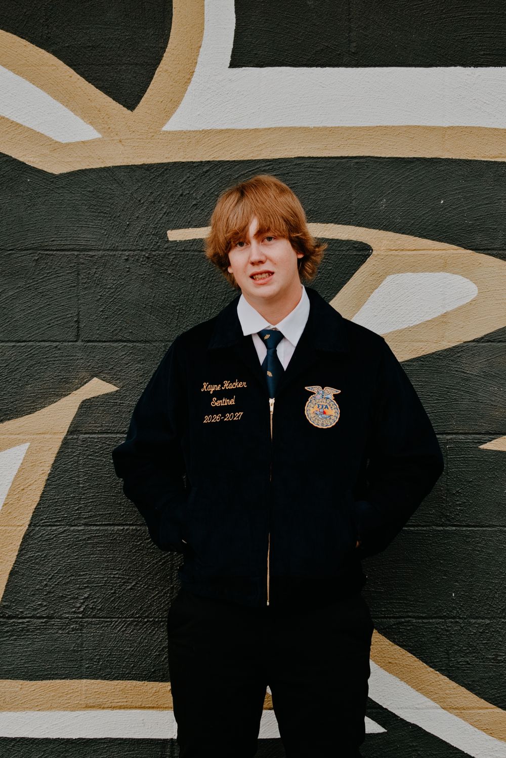Young man in FFA jacket smiling against a painted wall backdrop.