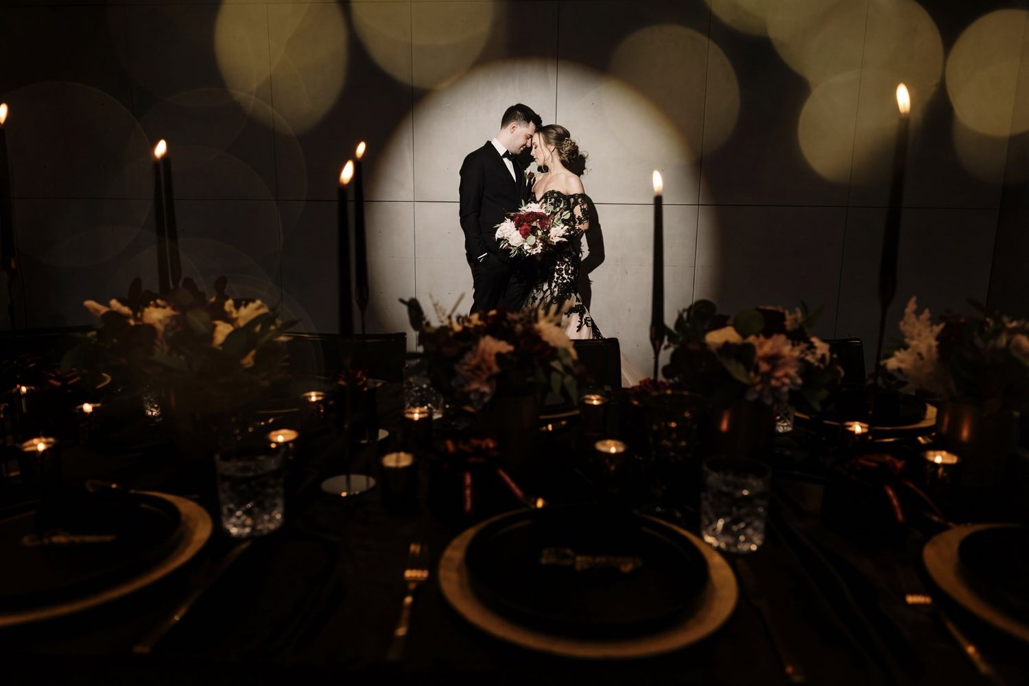 Bride and groom embracing in a spotlight behind candlelit reception tables at Mainspace