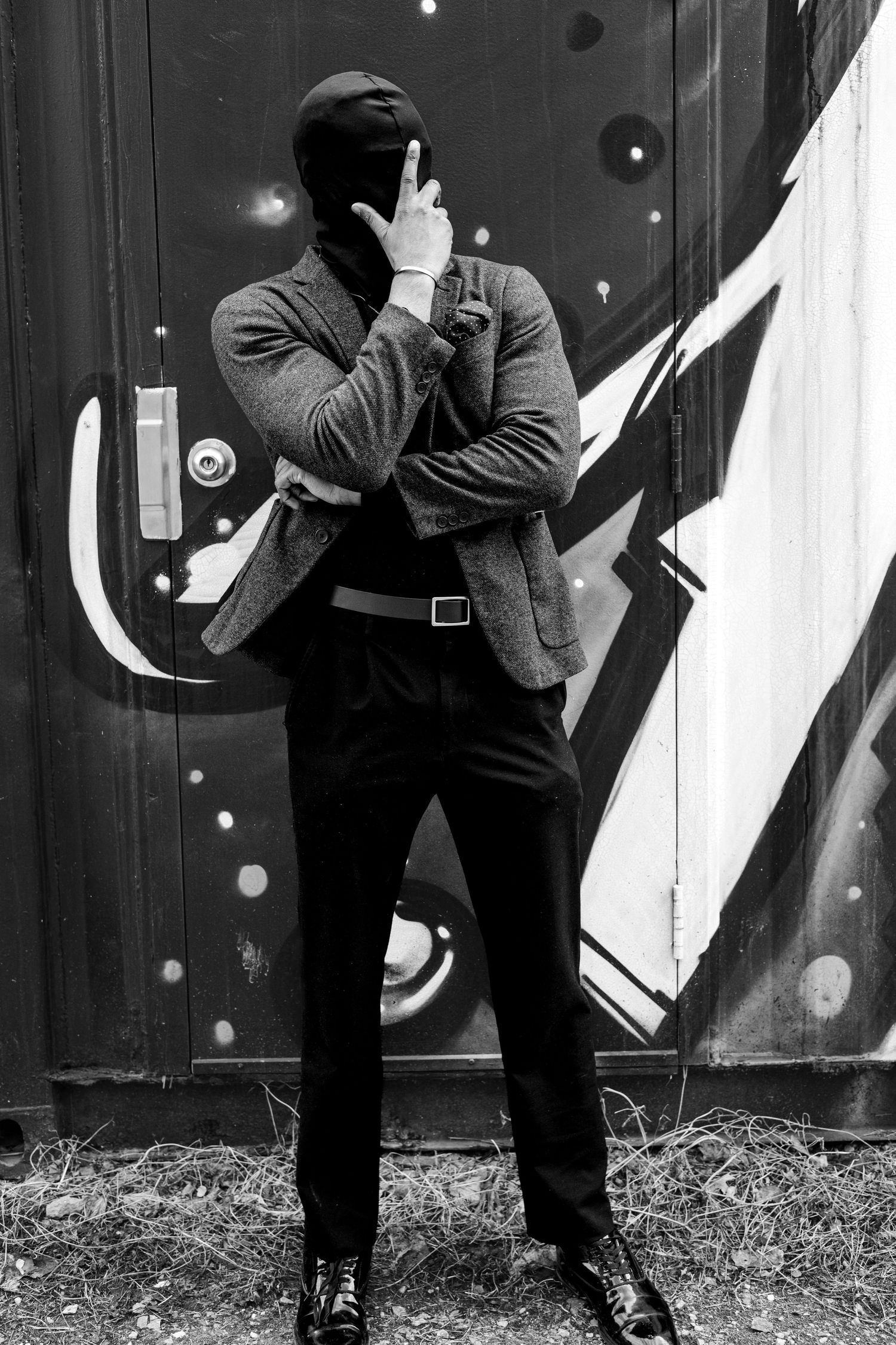 Black and white photo of a man standing beside a shipping container with 'Be Humble' graffiti mural.