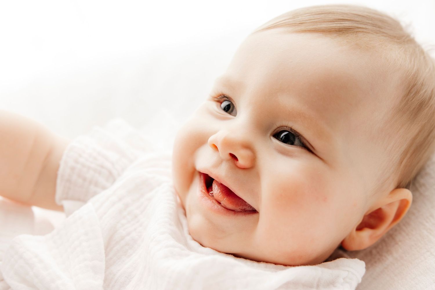 Adorable smiling baby with bright eyes lying on a soft white blanket, radiating joy and innocence.