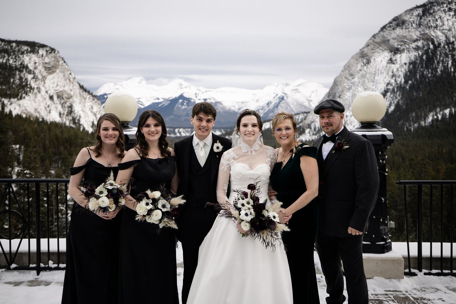 J + R with bridesmaids and loved ones on the snowy Fairmont Banff Springs terrace, snow-capped mountains behind