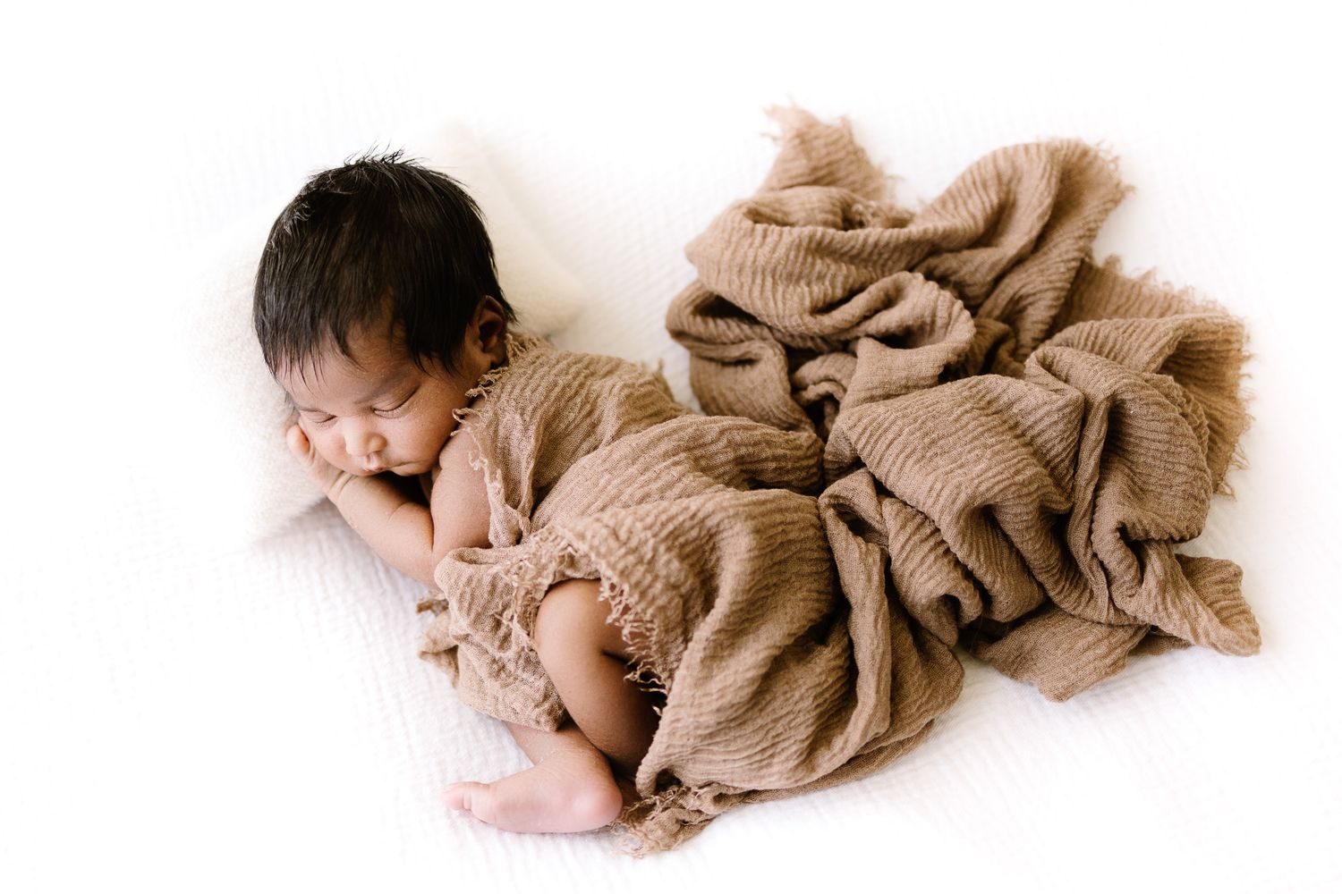 Adorable baby in white onesie doing tummy time on white background, looking at camera with curious eyes.