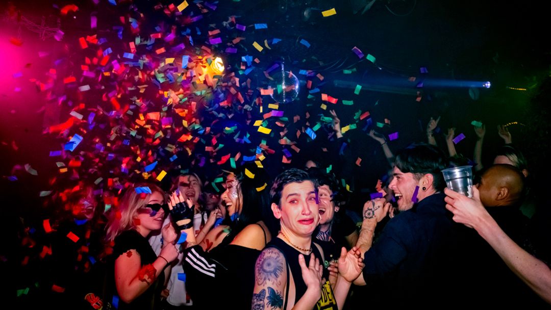 Colorful confetti rains over a crowd of young people dancing at a vibrant nightclub party.