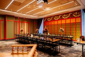 Elegant event room with long banquet tables, black chairs, floral centerpieces and red and gold Thai-inspired decor on the walls.
