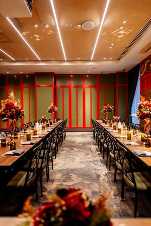 Elegant banquet room with long set tables, red floral centerpieces, green and red paneled walls, and modern linear ceiling lights.