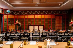 Elegant restaurant dining room with black chairs, wooden tables, fresh flower arrangements, and ornate red and green patterned walls.